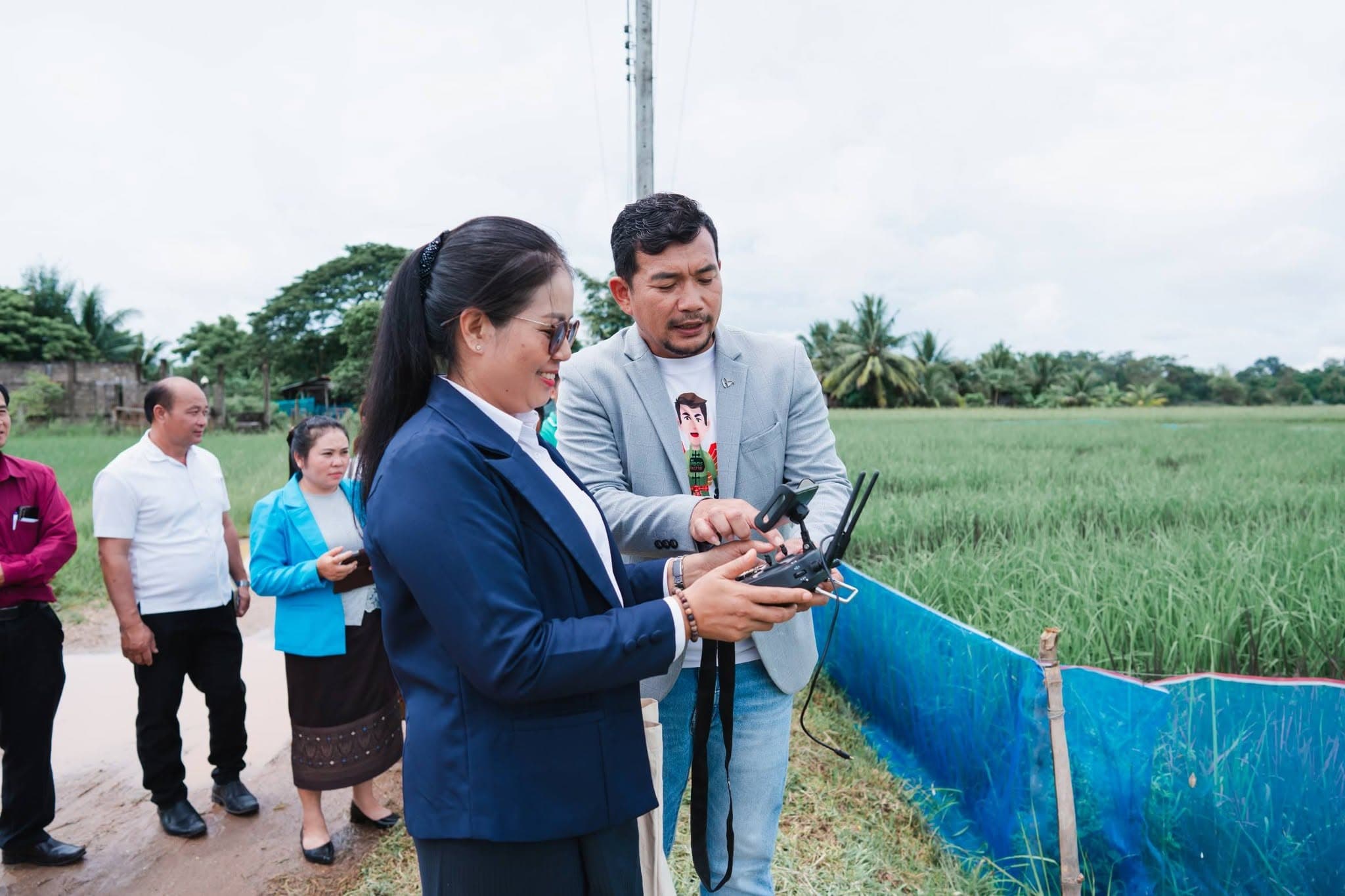หญิงสวมสูทสีกรมท่าจับรีโมตควบคุมโดรน ชายสวมสูทสีเทาชี้อธิบายปุ่มบนรีโมต