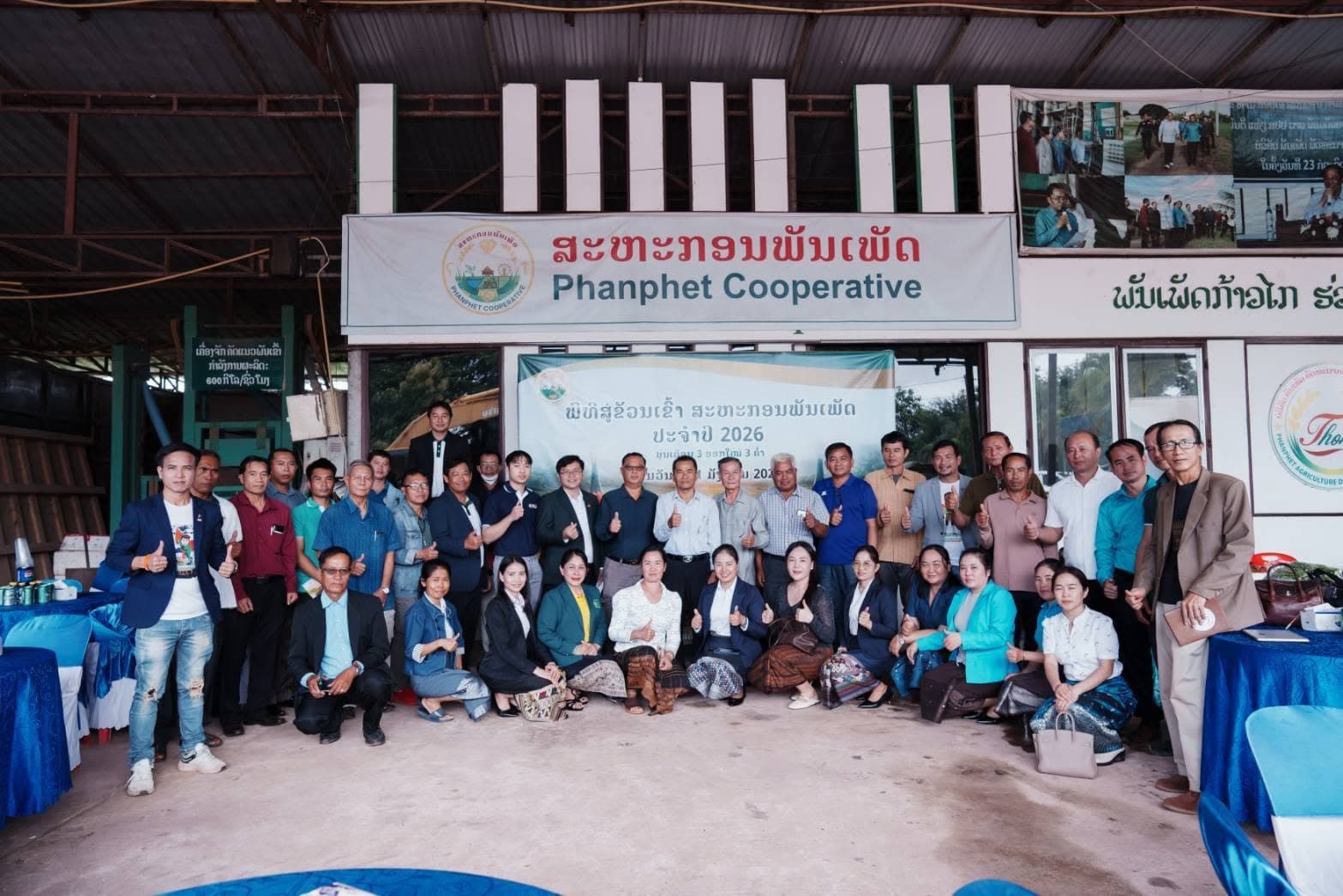 ภาพหมู่ผู้ร่วมงานหลายสิบคนหน้าอาคารสหกรณ์พันเพชร ใต้ป้ายชื่อสหกรณ์ภาษาลาวและอังกฤษ